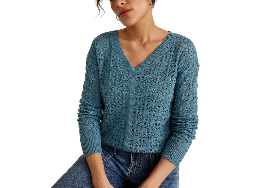 A woman is wearing a blue, long-sleeve V-neck crochet sweater with a geometric pattern, paired with blue jeans.