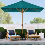 A large teal patio umbrella with a wooden pole and solar LED lighting along the ribs, surrounded by outdoor furniture by a poolside.
