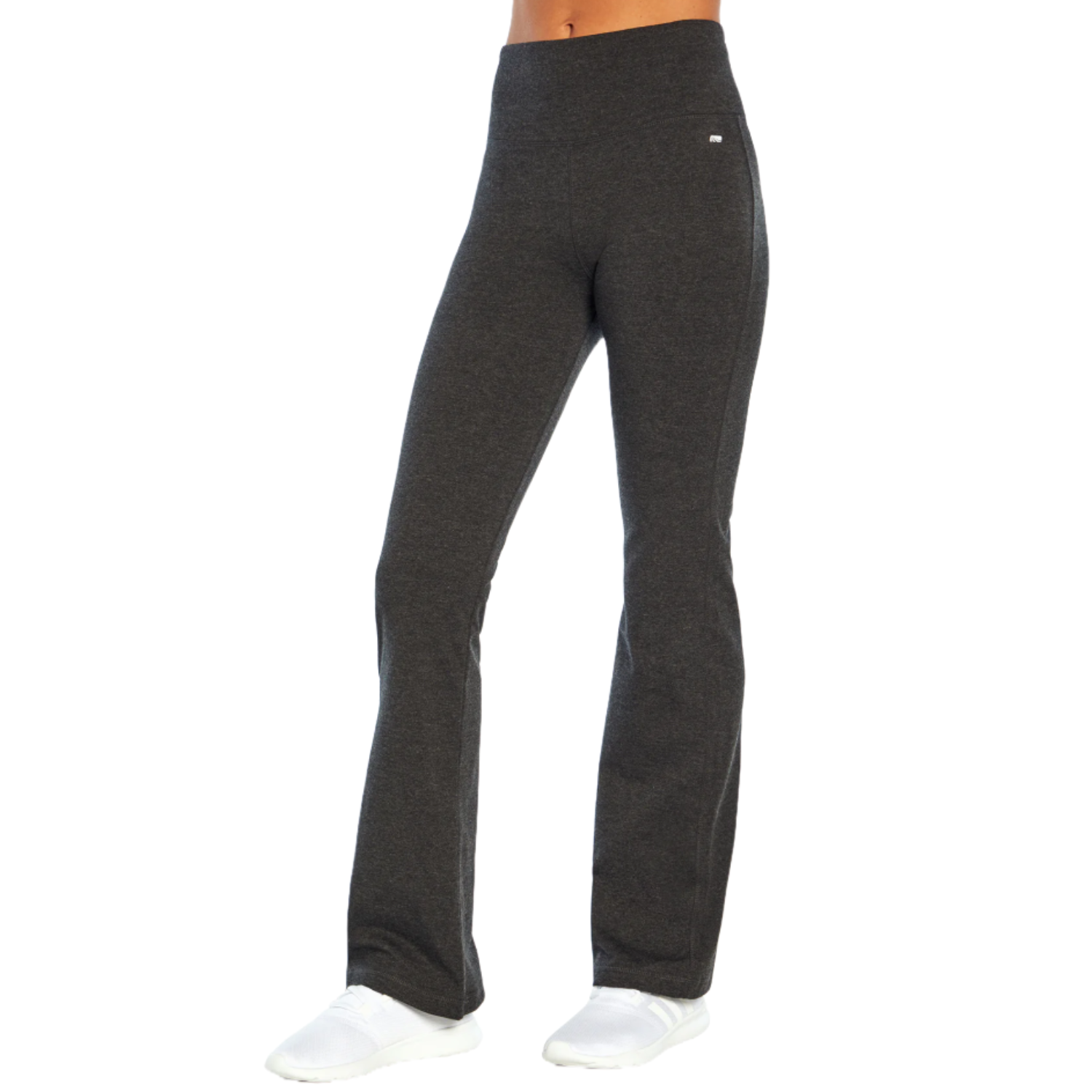 Marika Tummy Pants are dark gray, high-waisted yoga pants with a bootcut design, offering a sleek silhouette. They feature a small logo on the hip and are paired with white athletic shoes.