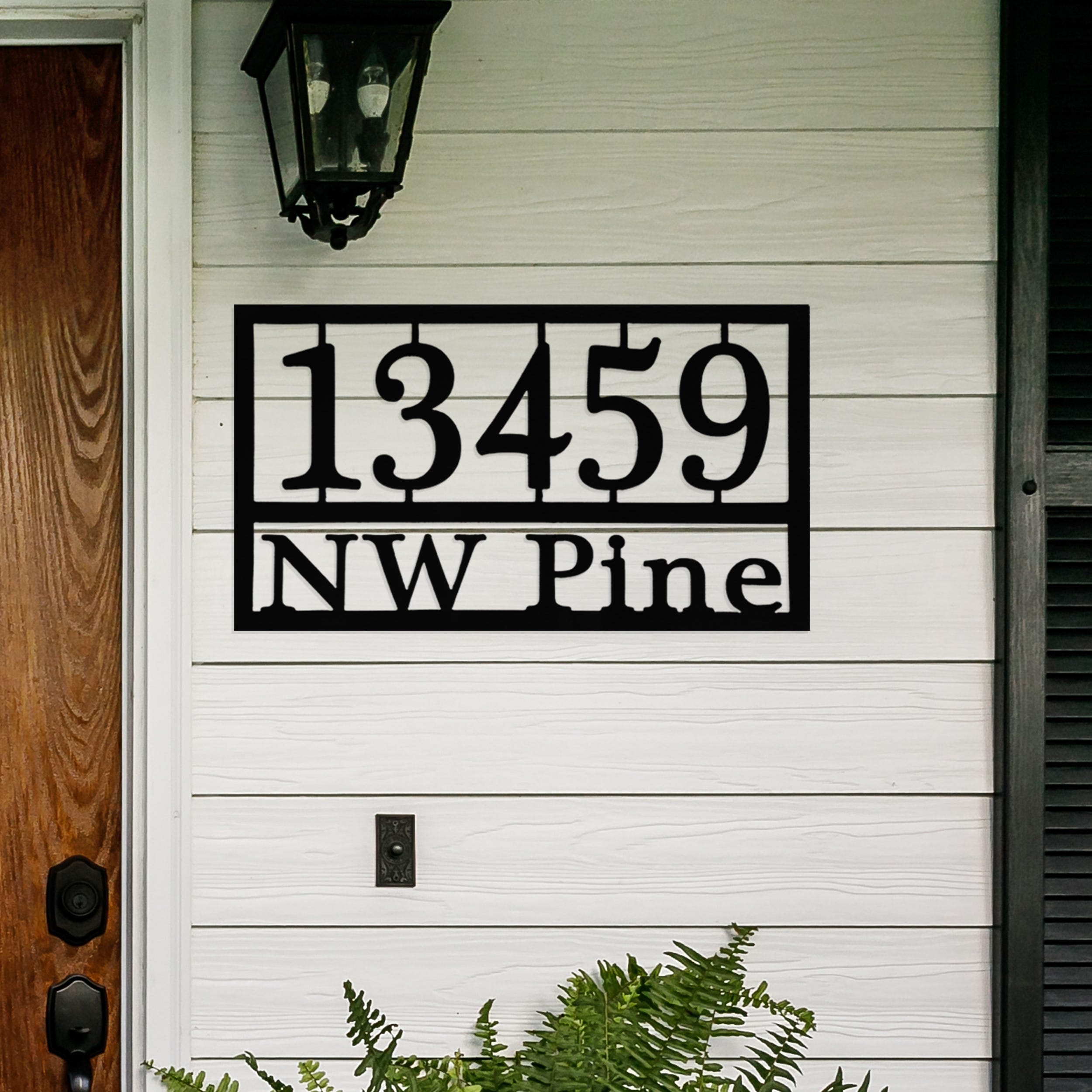 House number sign with the address \“13459 NW Pine\“ displayed on a white exterior wall, featuring black metal design.