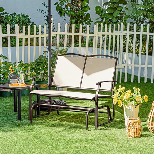 A two-person patio glider with a dark frame and light fabric, set against a white picket fence in a garden setting.