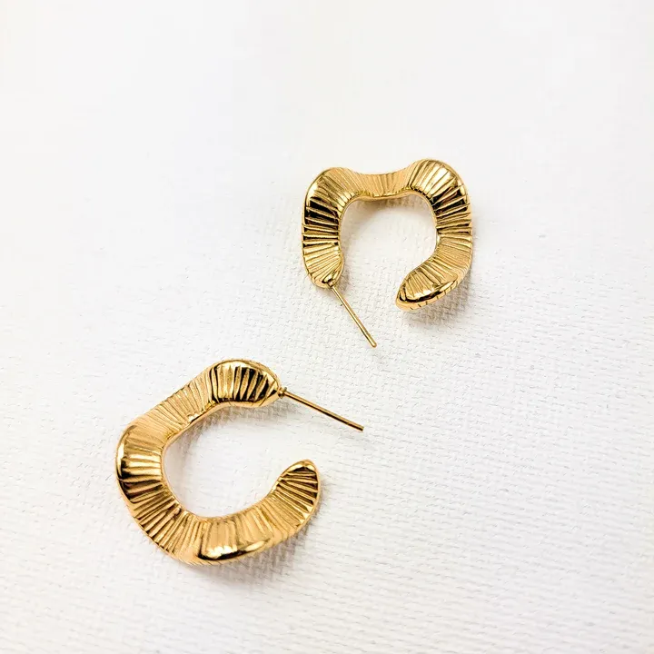 A pair of gold-tone, crescent-shaped hoop earrings with a ribbed texture.