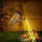 A solar-powered watering can decoration hangs on a shepherd's hook, casting a warm light through its patterned surface with strings of LED lights that create the illusion of pouring water.
