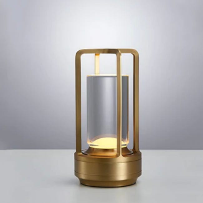 A contemporary golden lantern with a cylindrical frosted glass insert and a glowing, warm light.