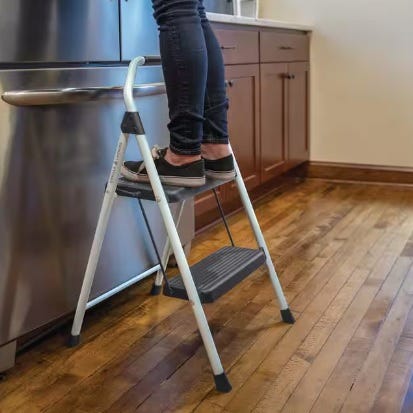 A step stool with a person standing on it in a kitchen setting.