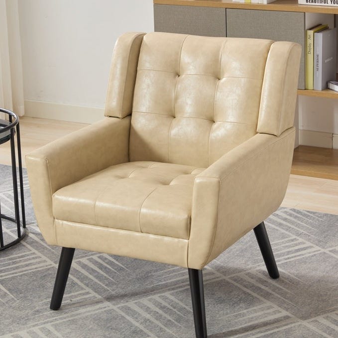 Beige tufted vegan-leather chair with a mid-century modern design, featuring a cushioned seat, high back, and slim black legs.