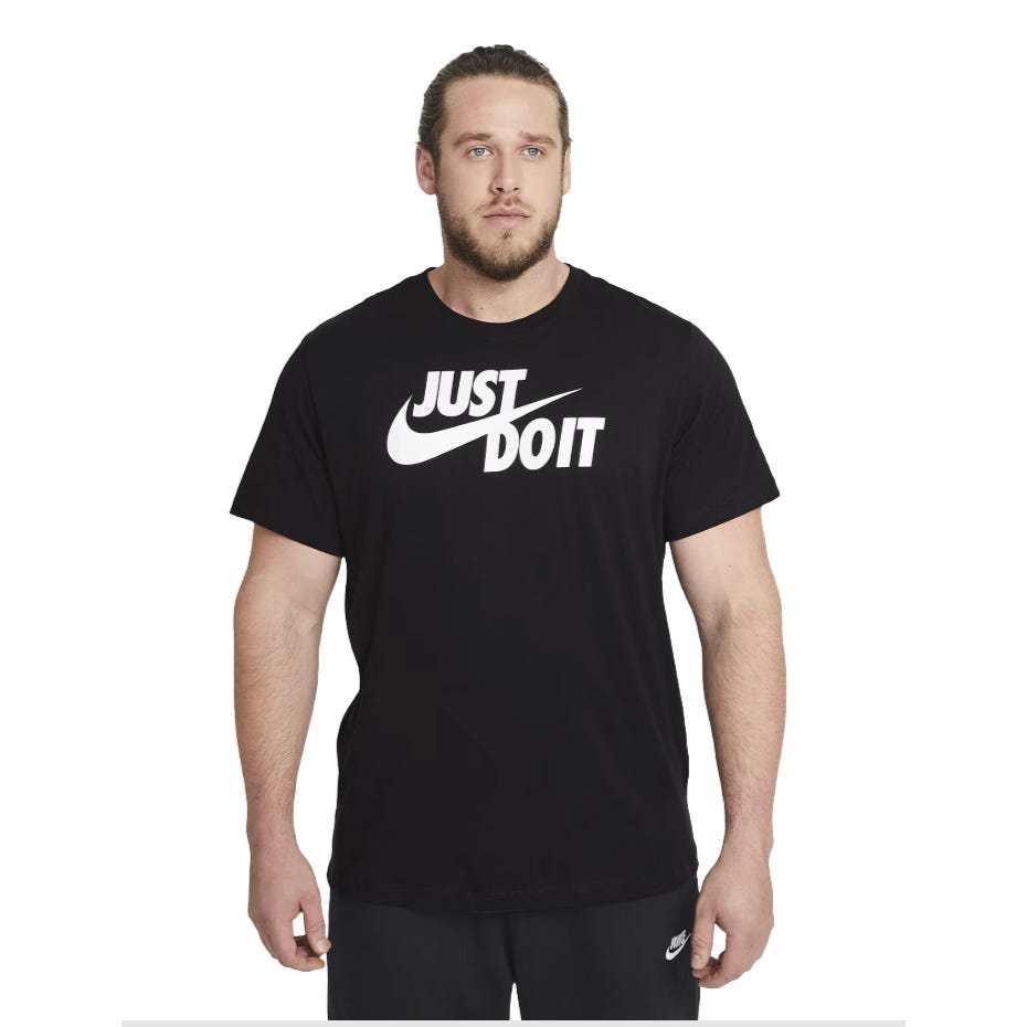 A man is wearing a black Nike t-shirt with the \“Just Do It\“ slogan in white on the front, paired with black Nike pants.
