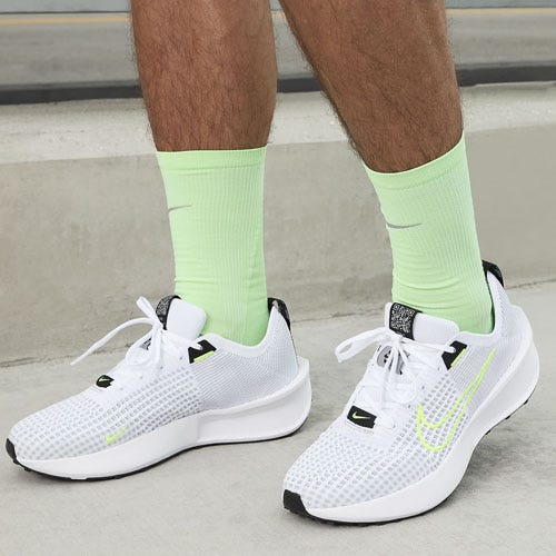 A person wearing white sneakers with neon accents and lime green crew socks.