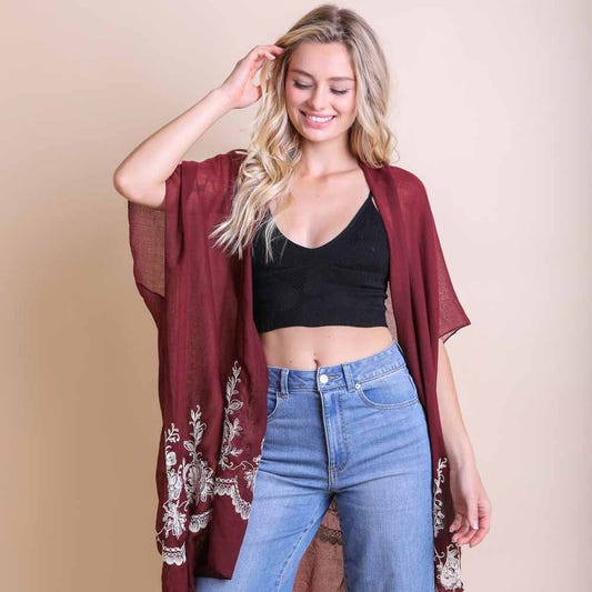 A woman wearing a maroon embroidered kimono, black crop top, and blue denim jeans.