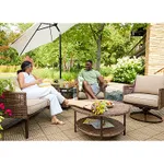 A rattan-style patio loveseat with cushioned seats and backrests is accompanied by a round coffee table and an armchair with matching design and cushions.