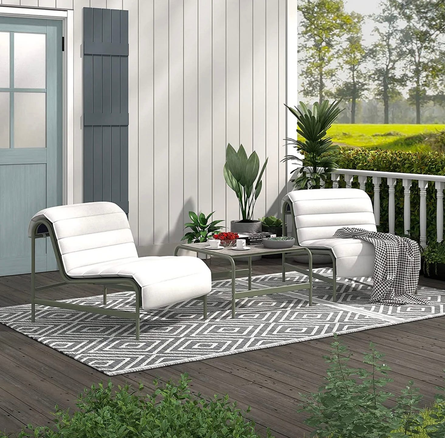 Two white lounge chairs with a matching side table on a patterned outdoor rug, placed on a wooden deck.