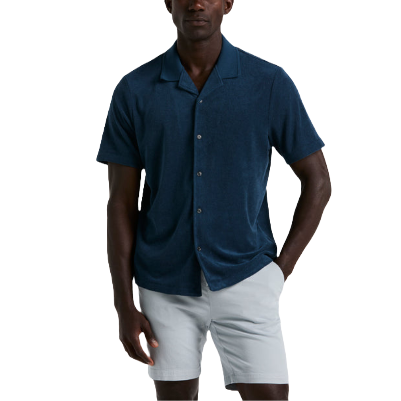 A man wears a dark blue Perry Ellis Camp Collar Shirt featuring short sleeves, button-down front, and a relaxed fit. Paired with light-colored shorts, it offers a casual and comfortable summer look.