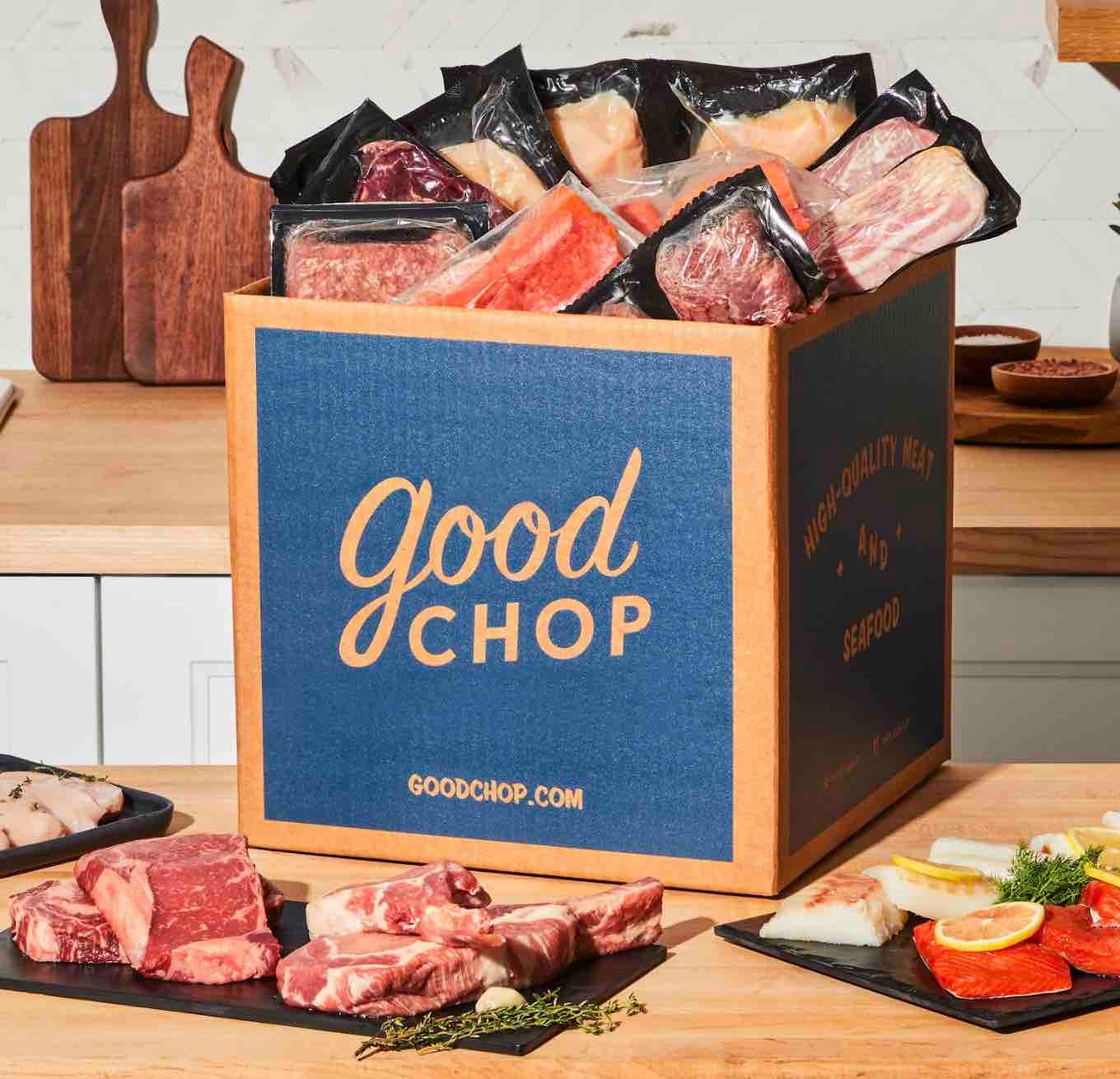Good Chop offers a delivery box containing various vacuum-sealed meats, including steaks and seafood, displayed on a wooden kitchen counter.