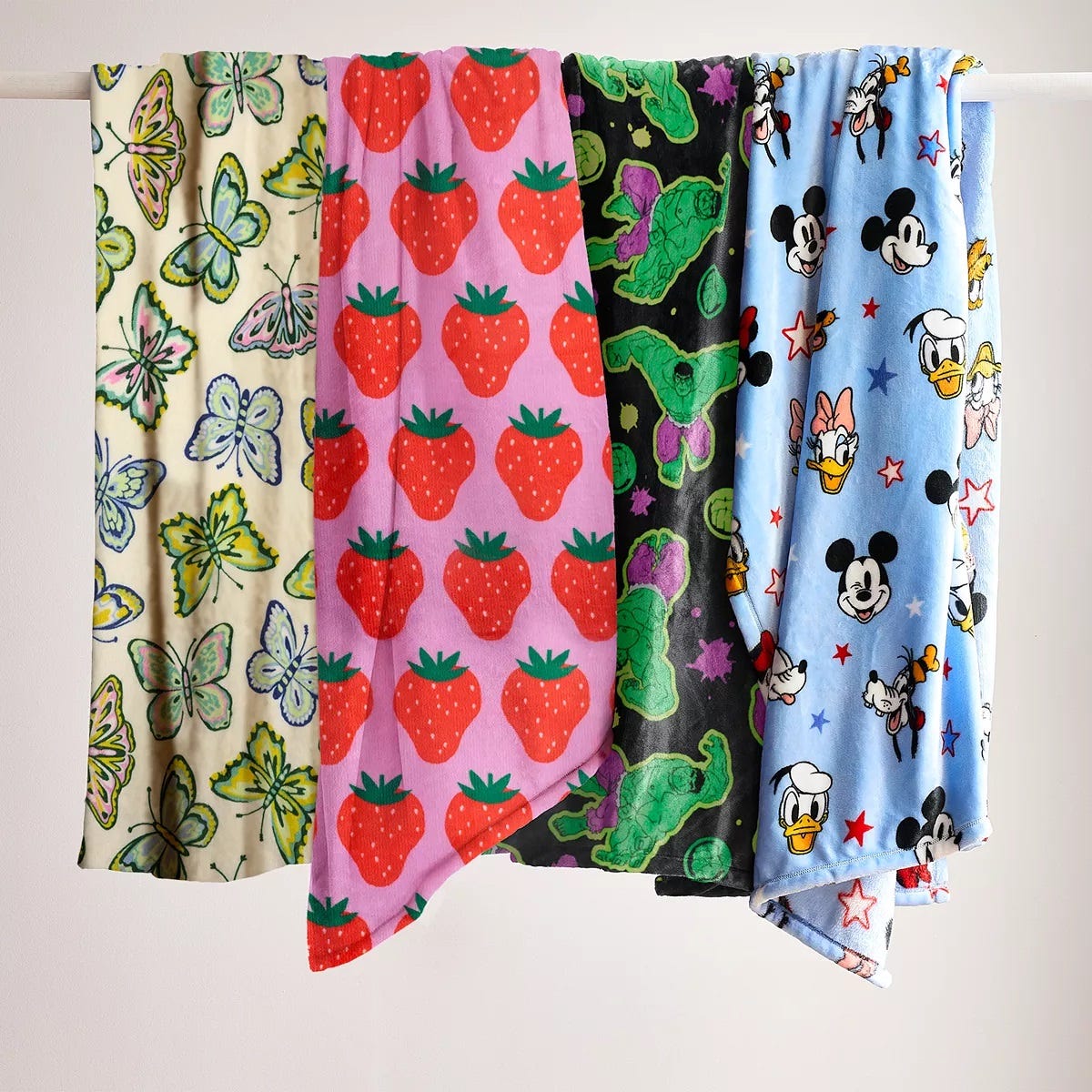 Four hanging textiles with different patterns: butterflies, strawberries, turtles, and cartoon characters.