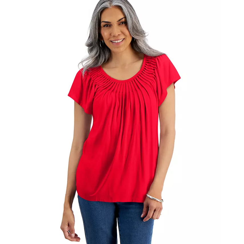 A woman is wearing a red, scoop-neck blouse with pleated detailing and short sleeves, paired with blue jeans.