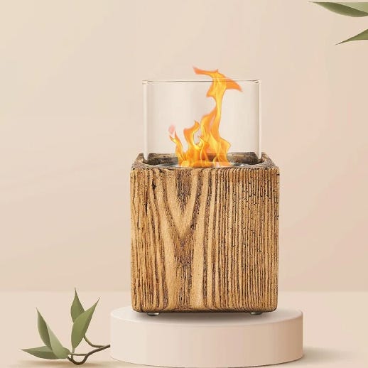 A tabletop bioethanol fireplace encased in a wood textured block with glass cylinder containing flames.