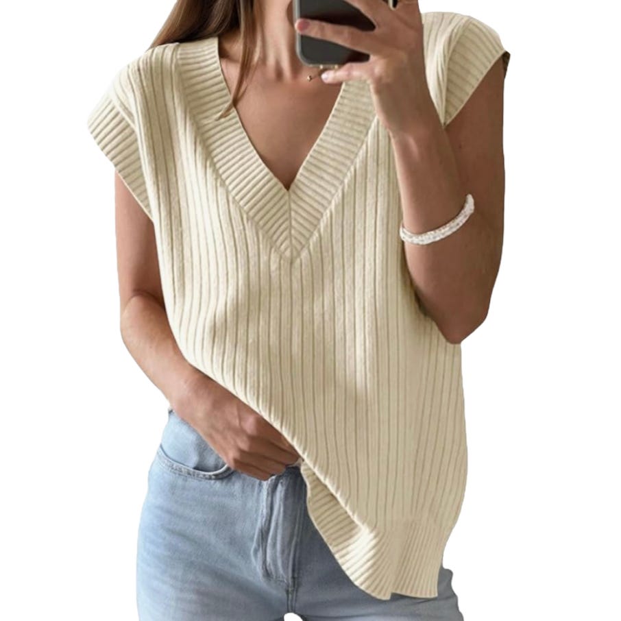A person is wearing a sleeveless, ribbed knit V-neck sweater in cream color, paired with light blue jeans.