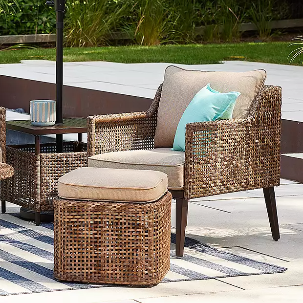 Rattan-style patio furniture set with two chairs, cushions, a side table, and an ottoman in an outdoor setting.