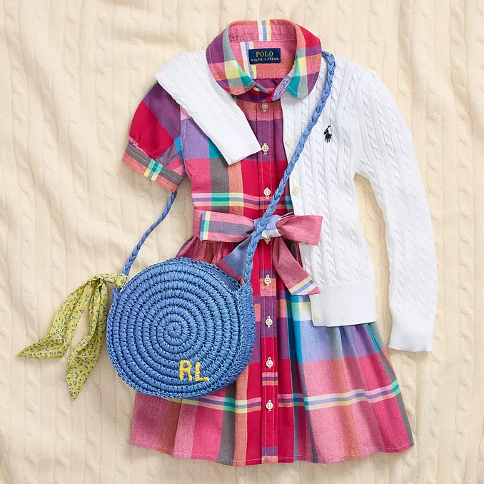 A multicolored plaid dress with a white cable knit cardigan and a round blue woven bag.