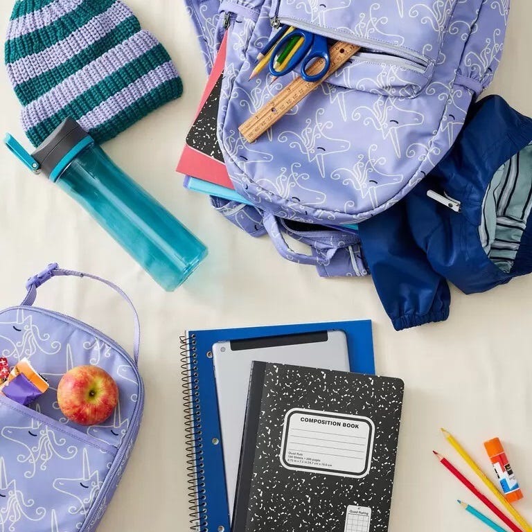 Backpack, notebooks, water bottle, scissors, ruler, pens, apple, knit hat, and a jacket are scattered on a surface.