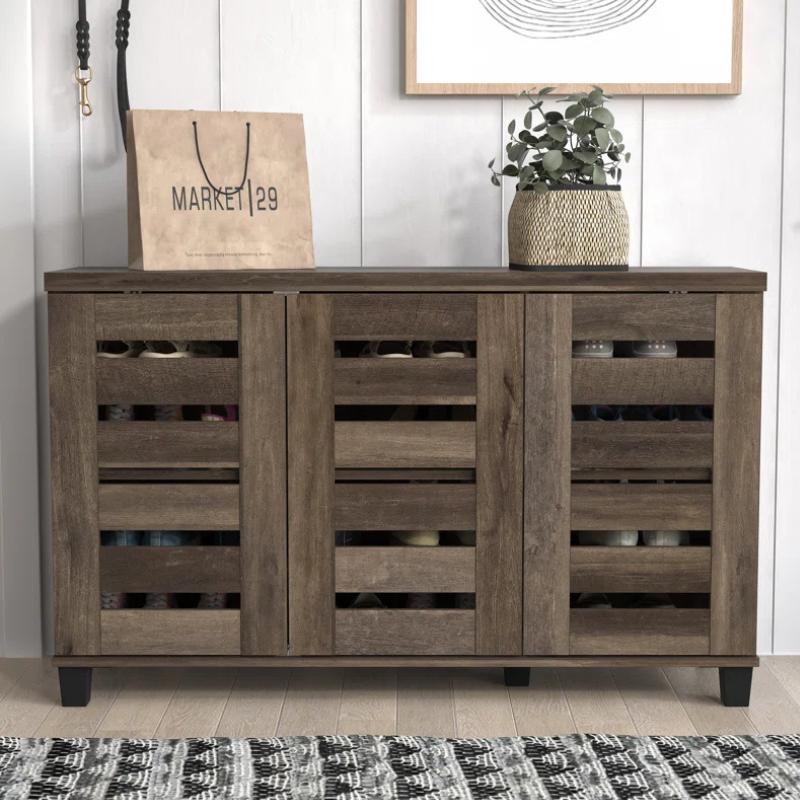 A wooden cabinet with slatted doors, set on a light wooden floor, features a decorative plant and a shopping bag labeled \“Market 129\“ on top.