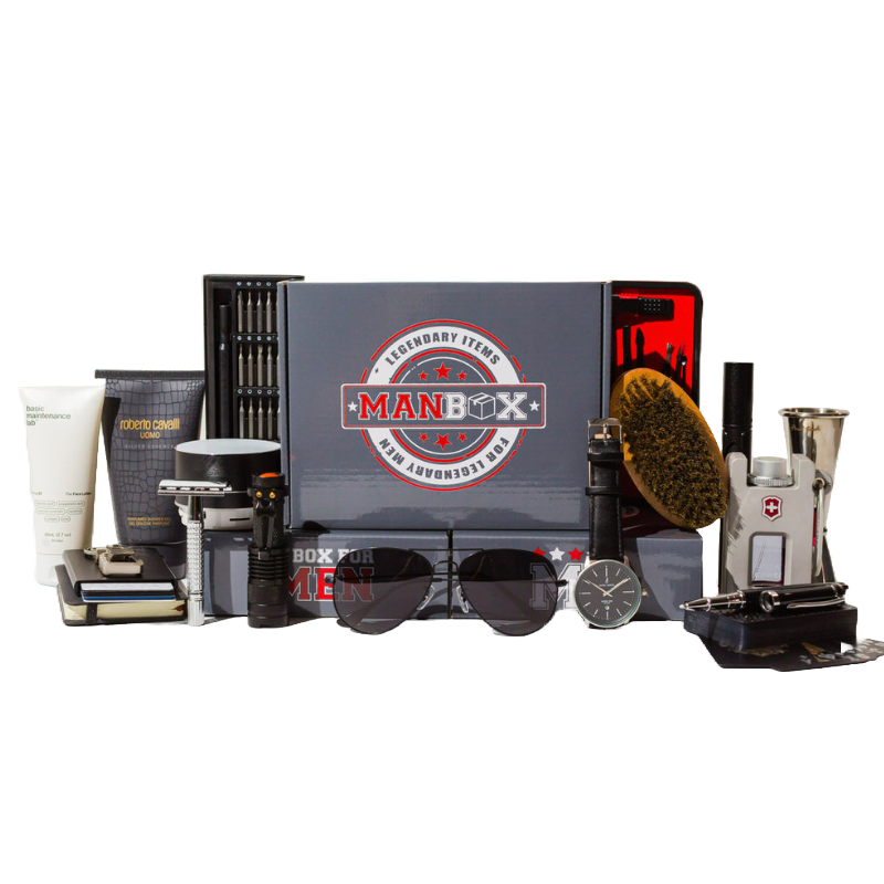 The Man Box contains grooming and lifestyle items like a shaving razor, sunglasses, watch, flashlight, screwdriver set, wristband, hairbrush, skin cream, and cologne, arranged in an aesthetically pleasing layout with a branded box.