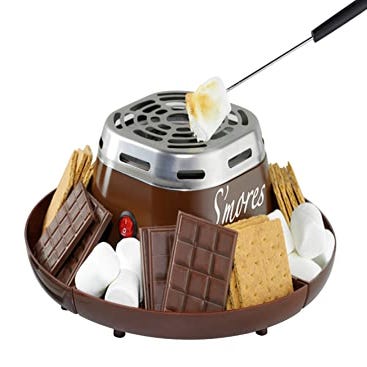 A tabletop s'mores maker featuring a round, grill-like center for roasting marshmallows, surrounded by compartments holding graham crackers, chocolate, and marshmallows.