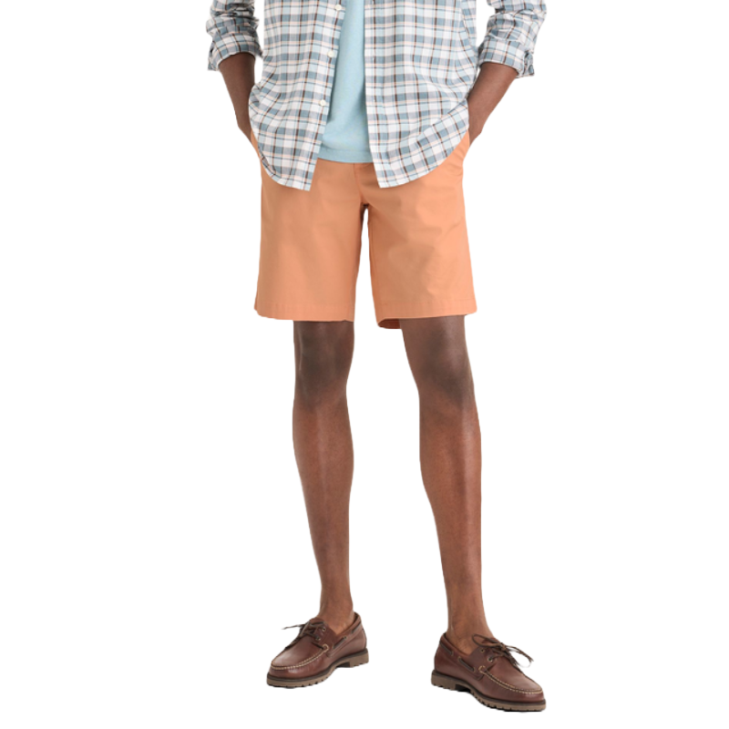 An outfit featuring peach-colored shorts paired with a light blue shirt and a plaid button-up shirt. The ensemble is completed with brown boat shoes.