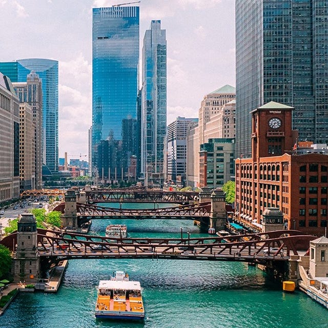 A scenic view of the Chicago River with bridges and boats, flanked by high-rise buildings and a historic clock tower.