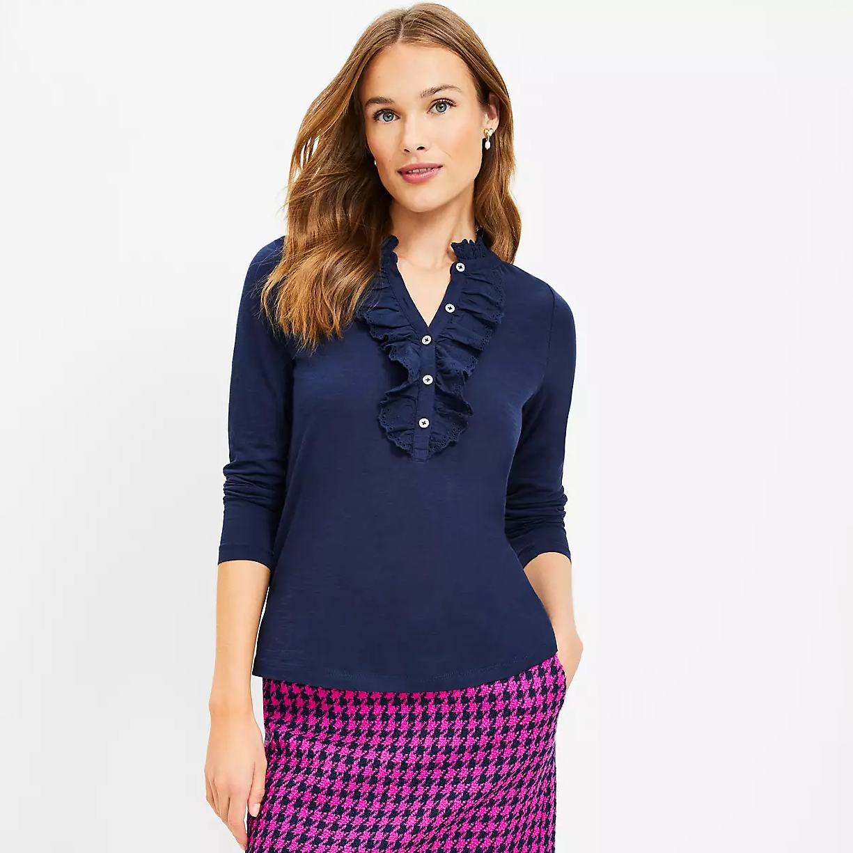 A woman is wearing a navy blue long-sleeve top with ruffle detail on the neckline and a pink and black houndstooth skirt.