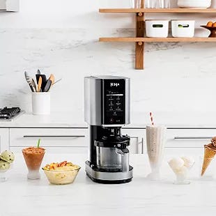 A coffee maker with a digital display is accompanied by four different types of desserts on a kitchen countertop.