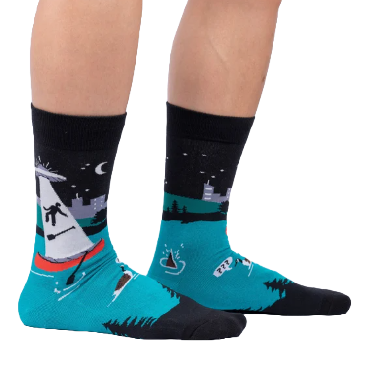 A pair of socks featuring a turquoise base with a black top, depicting a scene with a shark fin and silhouettes of birds flying over water.