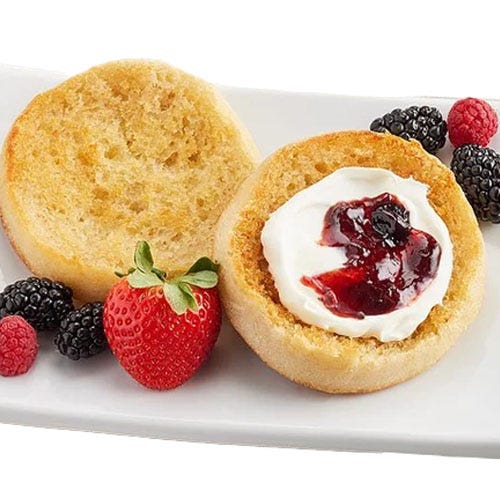 Wolferman's Super Thick English Muffins feature a toasted texture with a fluffy interior, topped with cream and berry jam, and are accompanied by fresh strawberries, blackberries, and raspberries on a white plate.