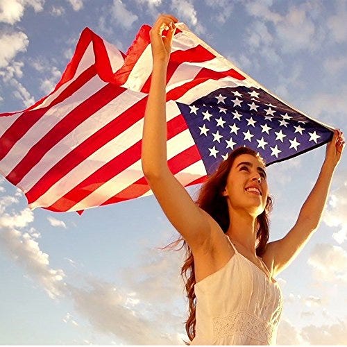 A woman is holding an American flag up towards the sky, showcasing the flag's stars and stripes in a clear, bright day.