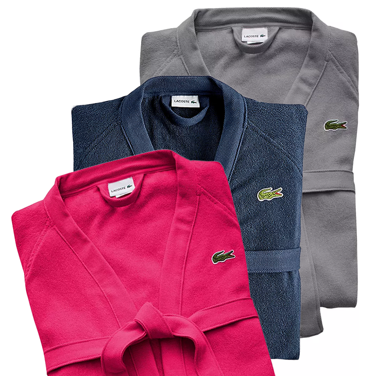 Three Lacoste bathrobes in blue, pink, and gray, each with the brand's crocodile logo.