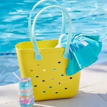 Yellow beach tote with blue towel and patterned insulated tumbler beside a pool.