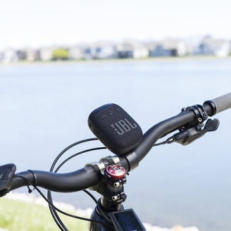 A portable speaker mounted on a bicycle handlebar next to a bell and a digital device.