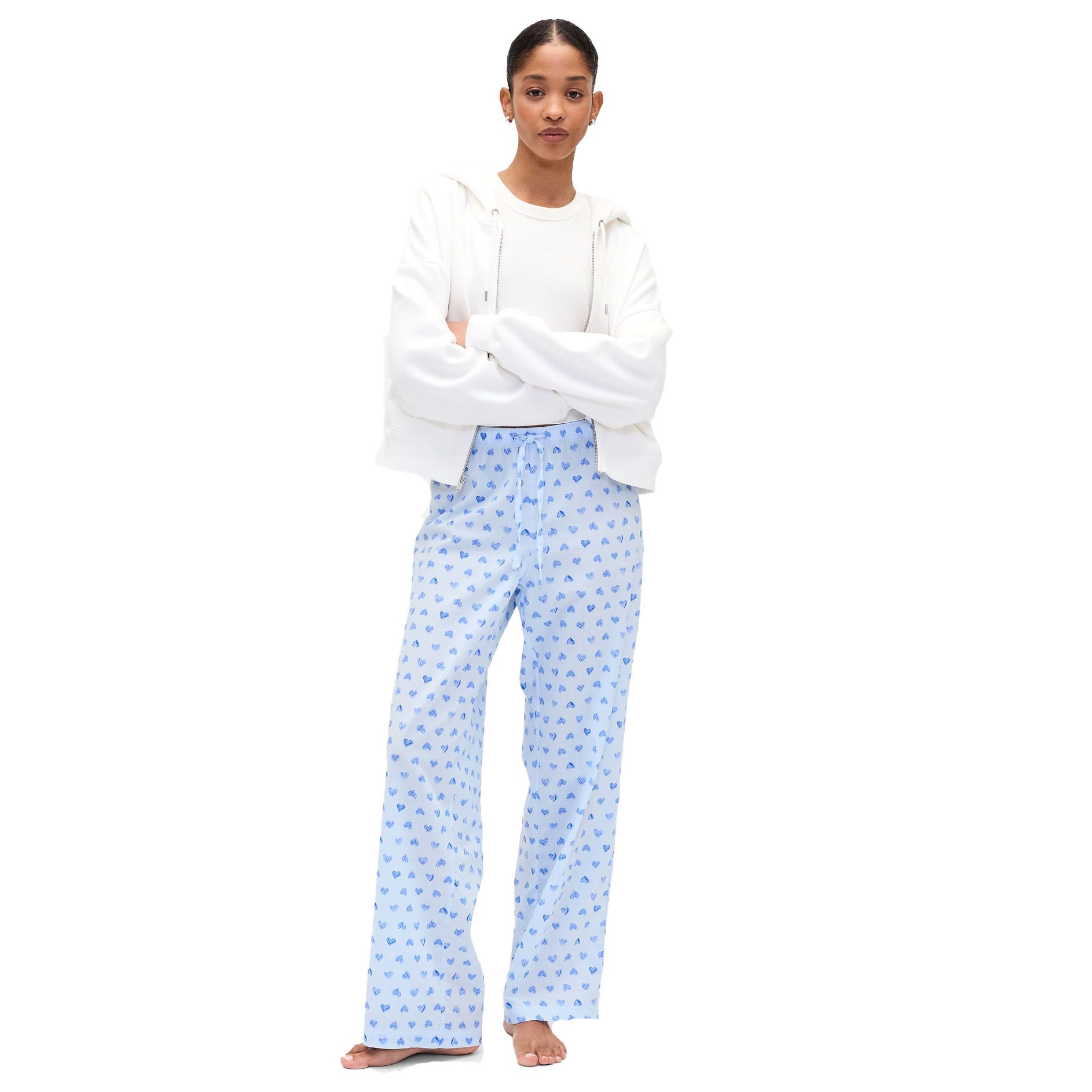 A person wearing a white hoodie and a white shirt with light blue pajama pants featuring a subtle heart pattern. The pants are loose-fitting and the outfit has a casual, comfortable style.