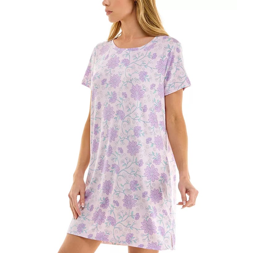 A woman is wearing a short-sleeve, knee-length dress with a purple floral pattern on a light background.