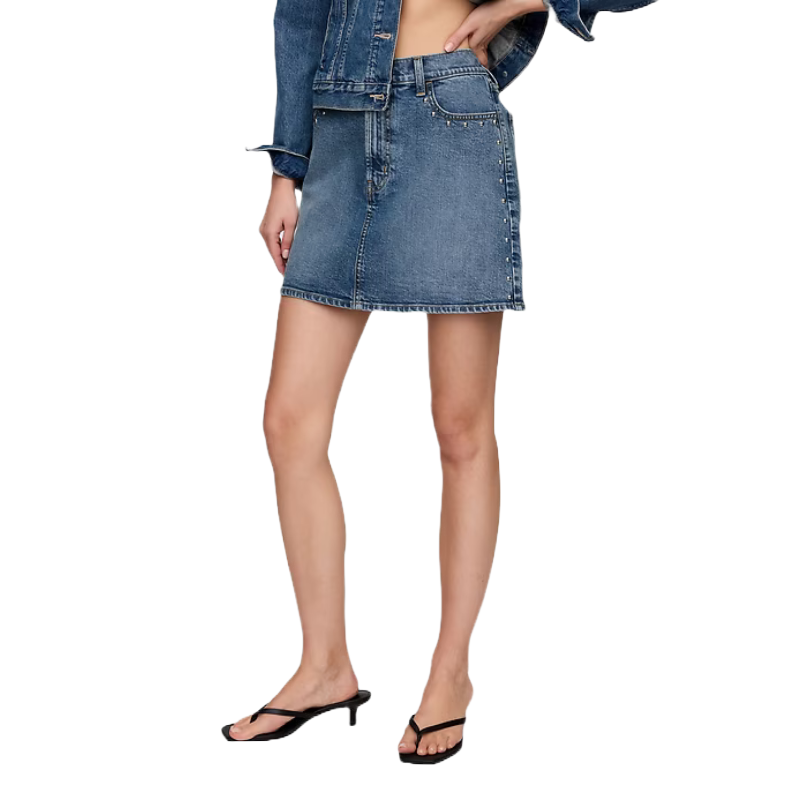 A model is wearing a denim A-line mini skirt paired with a denim jacket and black heeled sandals.
