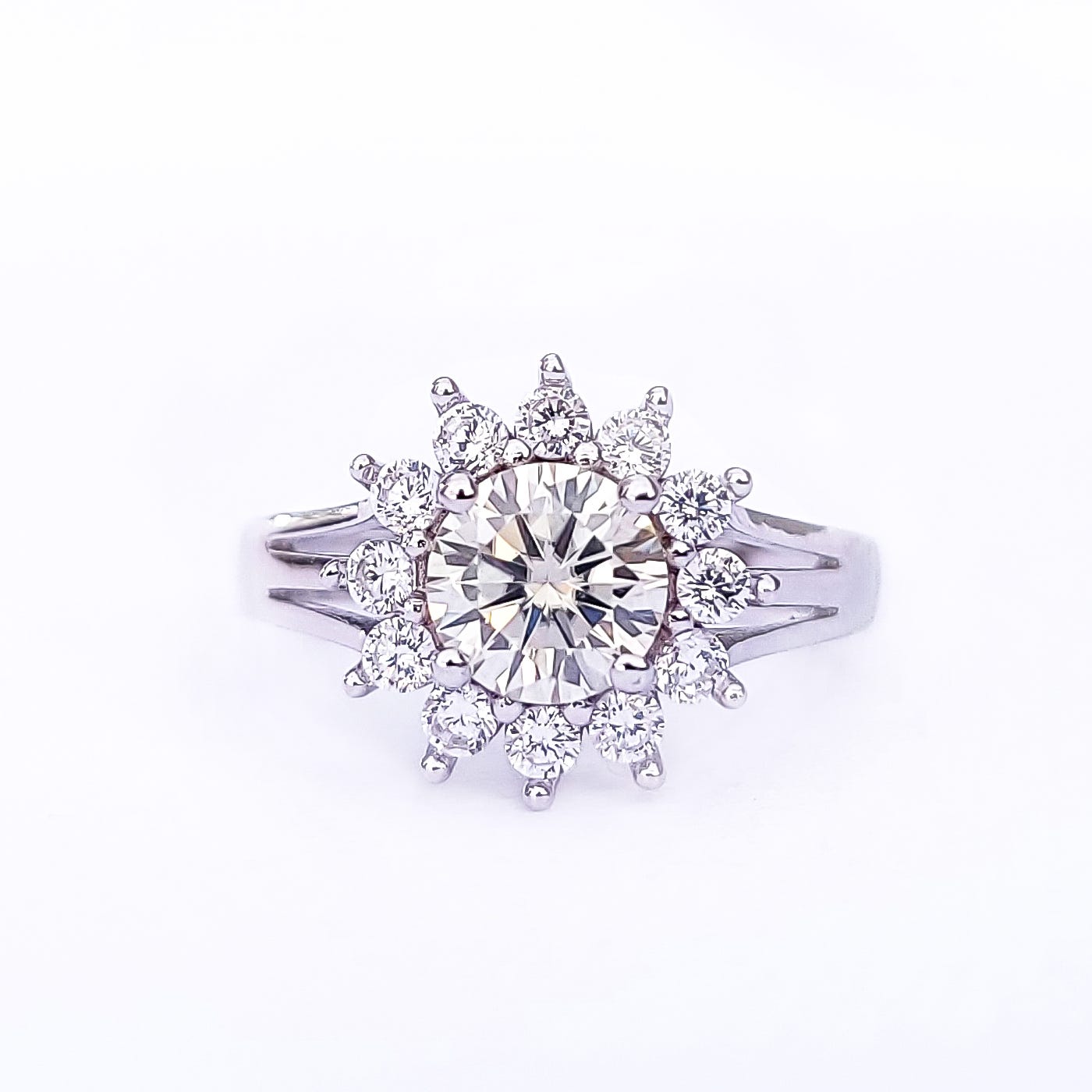 A diamond ring with a large central stone surrounded by smaller diamonds in a sunburst design, set in a silver-colored band.
