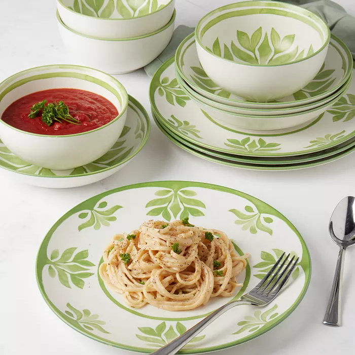 A set of green and white dinnerware with leaf patterns, including plates, bowls, and a pasta dish.