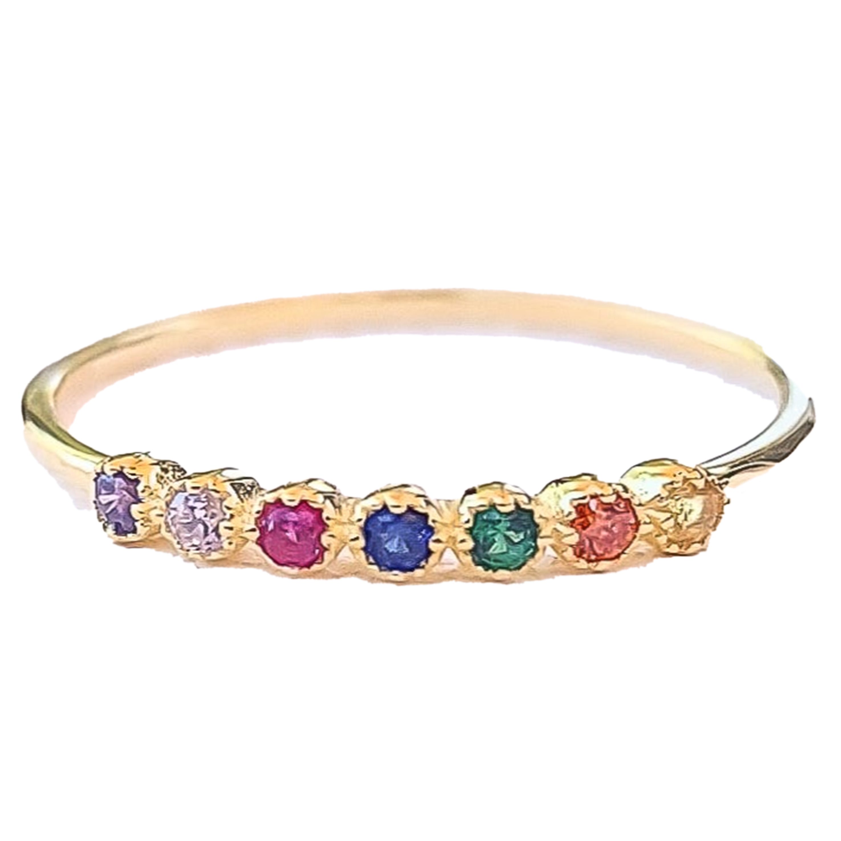 A thin gold-plated sterling silver ring featuring seven small, round, colorful cubic zirconia stones set in a row atop the band.