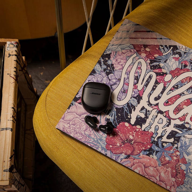 Wireless earbuds with a charging case, resting on a colorful notebook on a yellow surface.