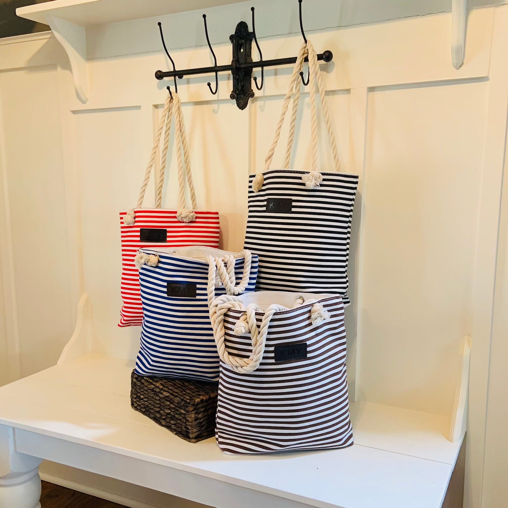 Striped tote bags with rope handles hanging on hooks against a white background.