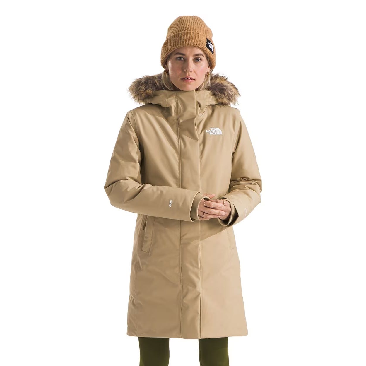 The North Face Arctic Down Jacket is a knee-length, tan coat with a fur-trimmed hood. It features a logo on the chest and is designed for warmth in cold weather.
