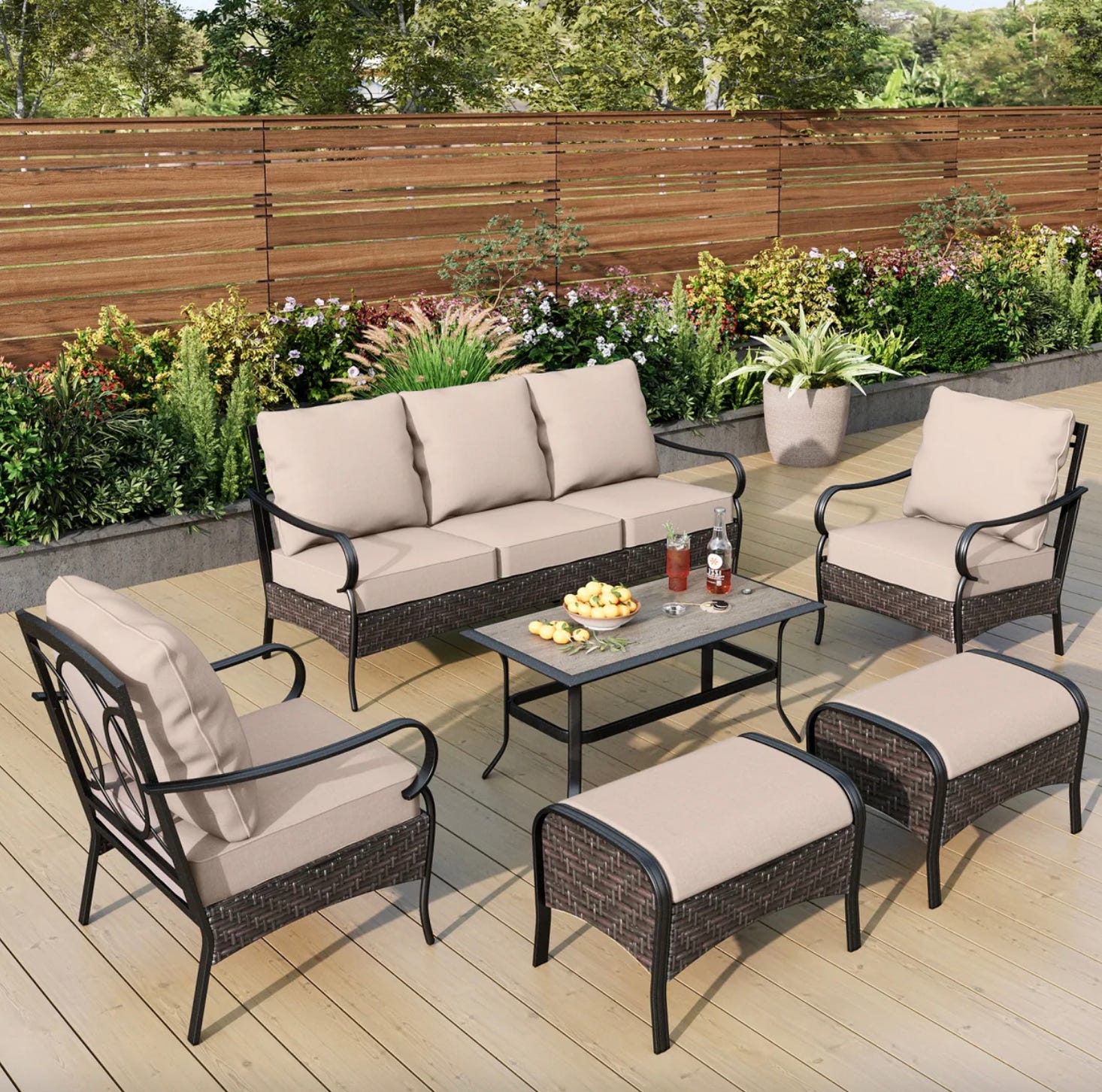 A 7-piece outdoor furniture set with a three-seat sofa, two armchairs, two ottomans, and a rectangular coffee table, all with beige cushions and dark rattan-style frames.