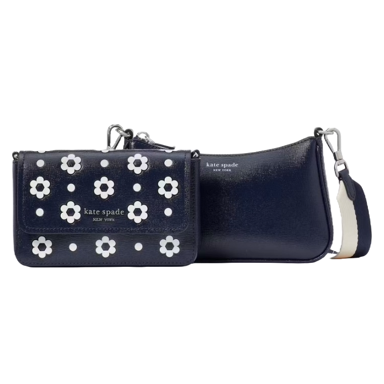 Kate Spade Double Up Daisy Dot Crossbody features two navy bags, one with white daisy embellishments and the other plain. Both have detachable straps, allowing versatility in carrying options.