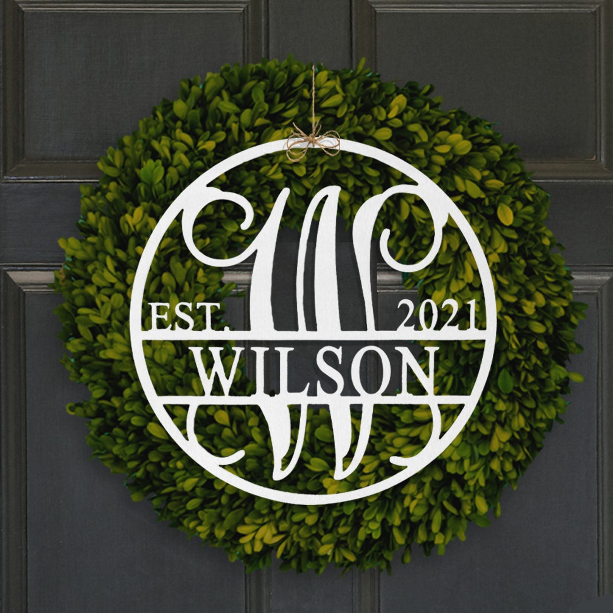 A green leafy wreath with a personalized white monogram sign featuring a family name and established year.