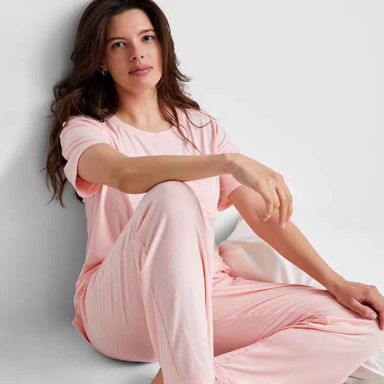 A woman is wearing a light pink, striped pajama set consisting of a short-sleeved top and pants.